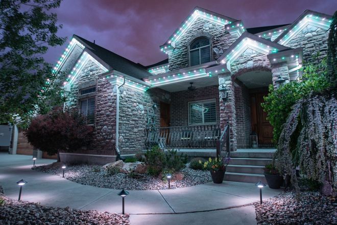 The front of a stone home lit in cool white, walkway lights on