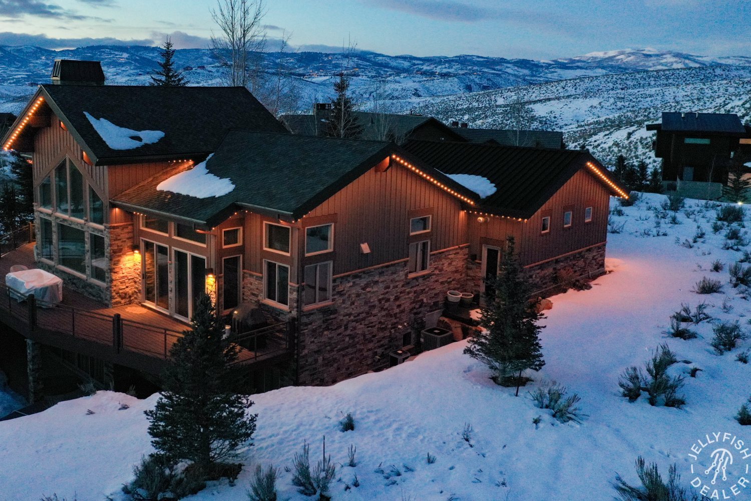 A large home with every roofline in warm white at dusk, snow on the ground